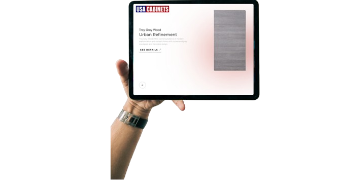 A hand holding a tablet. On the screen of the tablet there is the USA Cabinets logo at the top left, and on the main section of the screen there is a picture of a cabinet door with text beside it that describes the cabinet.